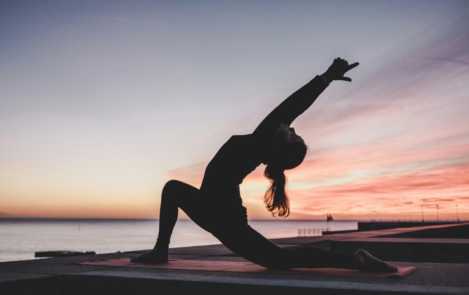 A silhouetted low lunge on a seafront at sunset